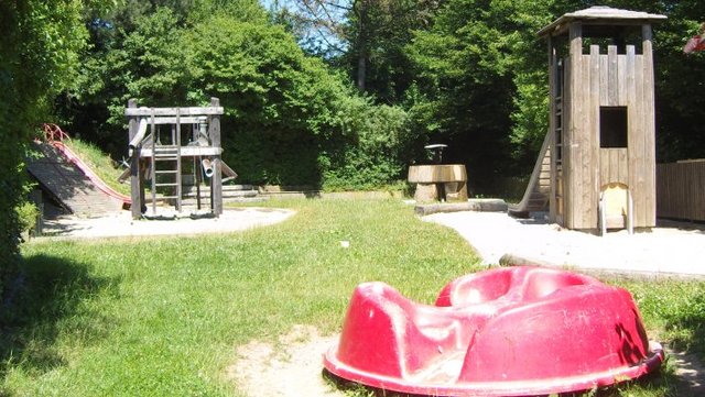 Vorne ist ein Sandkasten, hinten links eine Rutsche und ein Spielturm und rechts ein Kletterturm mit Rutsche